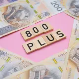 Drewniane klocki z napisem "800 PLUS" na tle polskich banknotów 200 zł.