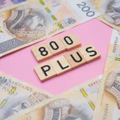 Drewniane klocki z napisem "800 PLUS" na tle polskich banknotów 200 zł.