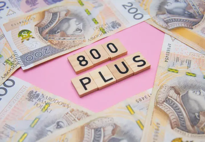 Drewniane klocki z napisem "800 PLUS" na tle polskich banknotów 200 zł.