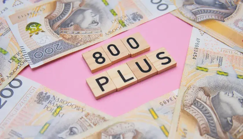 Drewniane klocki z napisem "800 PLUS" na tle polskich banknotów 200 zł.