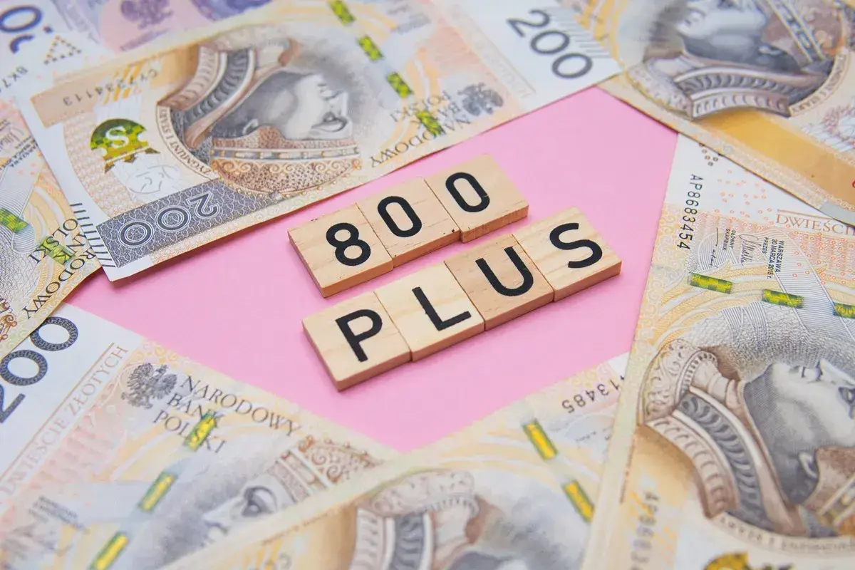 Drewniane klocki z napisem "800 PLUS" na tle polskich banknotów 200 zł.